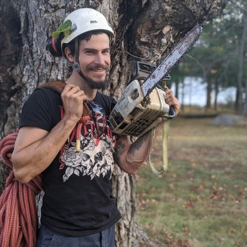 An image of Christian Grigoraskos wielding a chainsaw and carrying other tools.