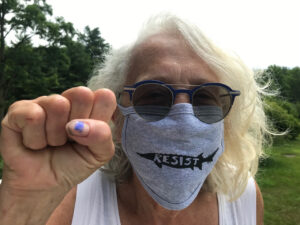 An action shot of Branda Miller, with her fist raised wearing a mask and sunglasses.