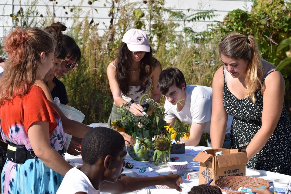 Two people are looking at and examining a plant, the woman on the left is touching it and the man on the right is leaning down to watch.
