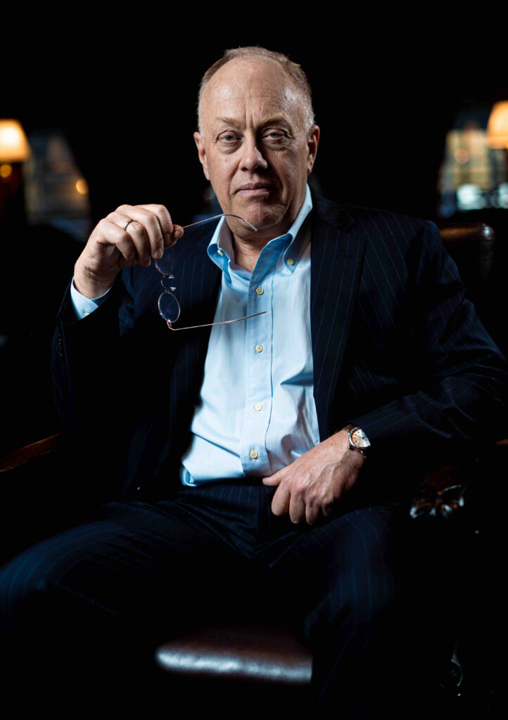 Head shot of author Chris Hedges seated holding his glasses
