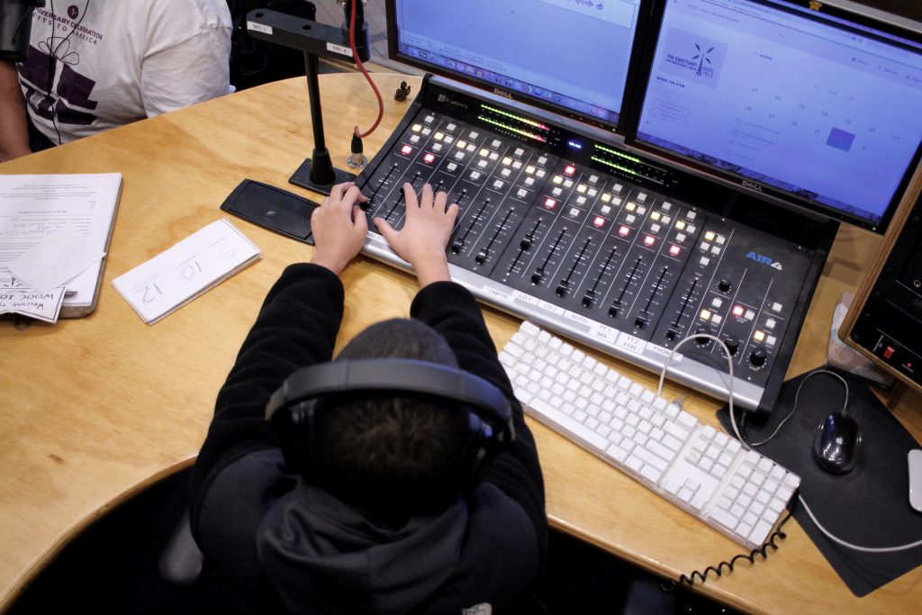 a picture from above of a young person using the sound board and computer in the radio studio
