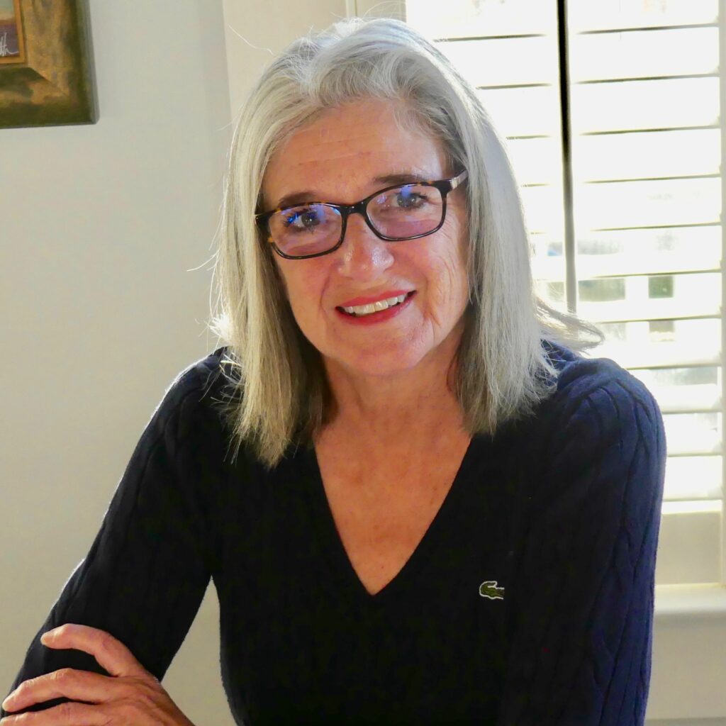 A headshot of Noreen McKee, who has medium-length white hair and glasses, wearing a a dark purple sewater.