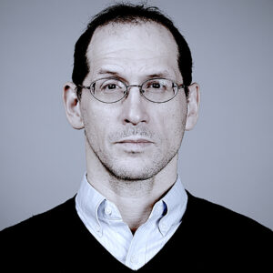 A headshot of Noah Potter, who is wearing glasses and a button-up under a sweater.