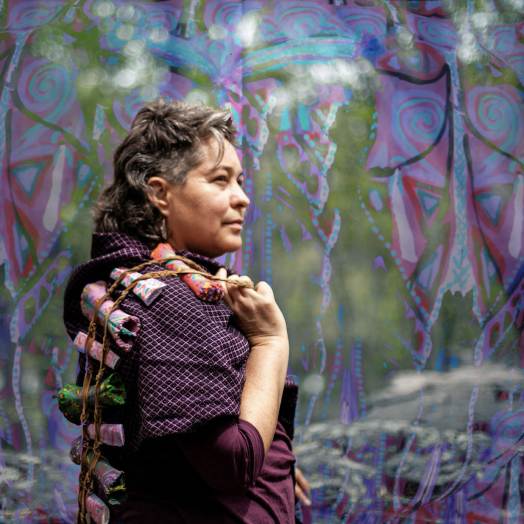 An image of Géraldine Eguiluz in front of a colorful piece, wearing a purple shirt with her hair pulled back.