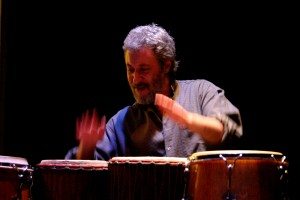 Adam Rudolph in performance, playing four drums with hands.