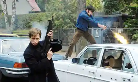 Screen grab from "The Baader Meinhof Complex." A young man holding a machine gun up to the sky. A man behind him is standing on the roof of a car using a blow torch.