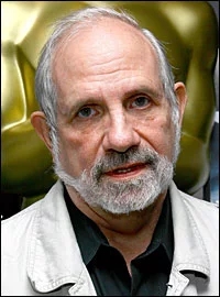 A headshot of Brian De Palma, wearing a black shirt under a white blazer in front of a gold background. 