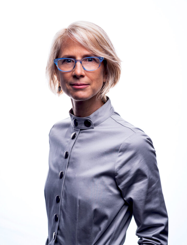 A medium-framed headshot of Heidi Boisvert, who has short blonde hair and is wearing blue glasses and a blue blouse.