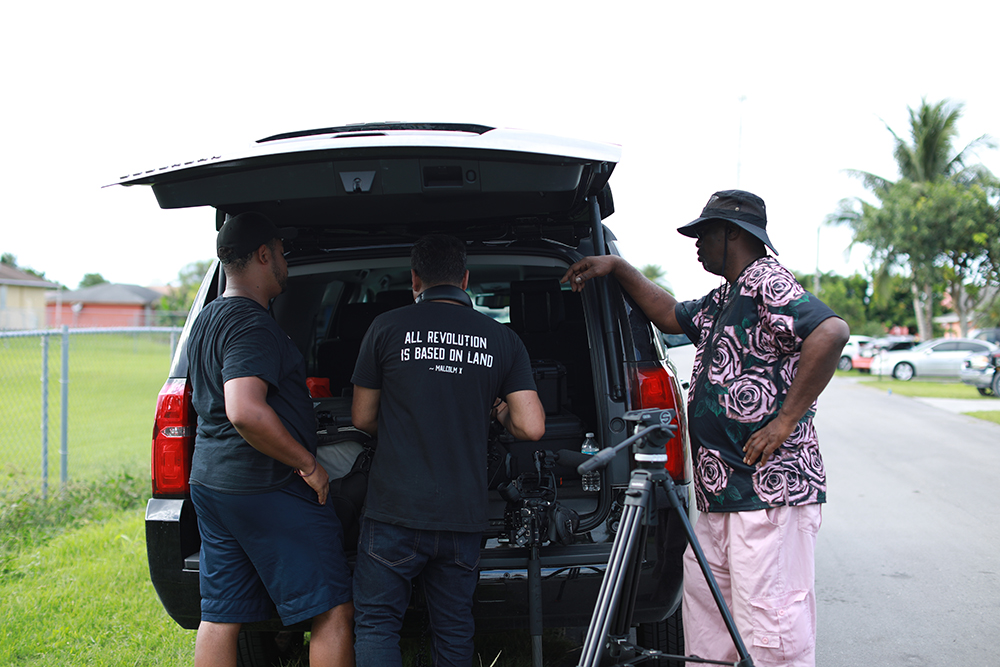 An action shot of the filming process for Outta The Muck gathered around the trunk of a car.
