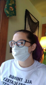 A picture of Eileen Raab, a white woman with brown hair pulled back in a ponytail. She is wearing glasses, a white mask, and a white t-shirt.