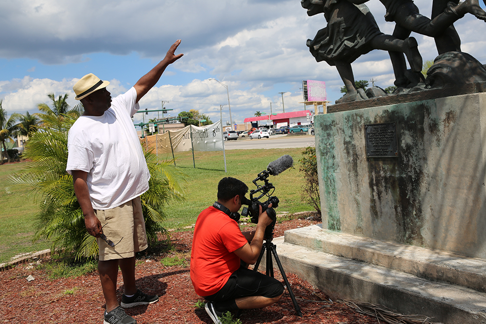 An action shot of the filming process for Outta The Muck in front of a statue.