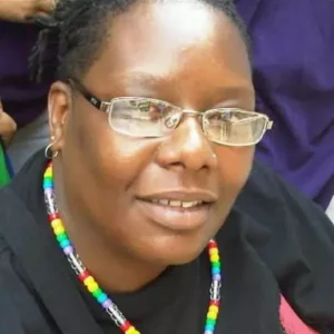A headshot of Roni Minter, an African American woman. She is wearing glasses, a black shirt, and a colorful beaded neckless.