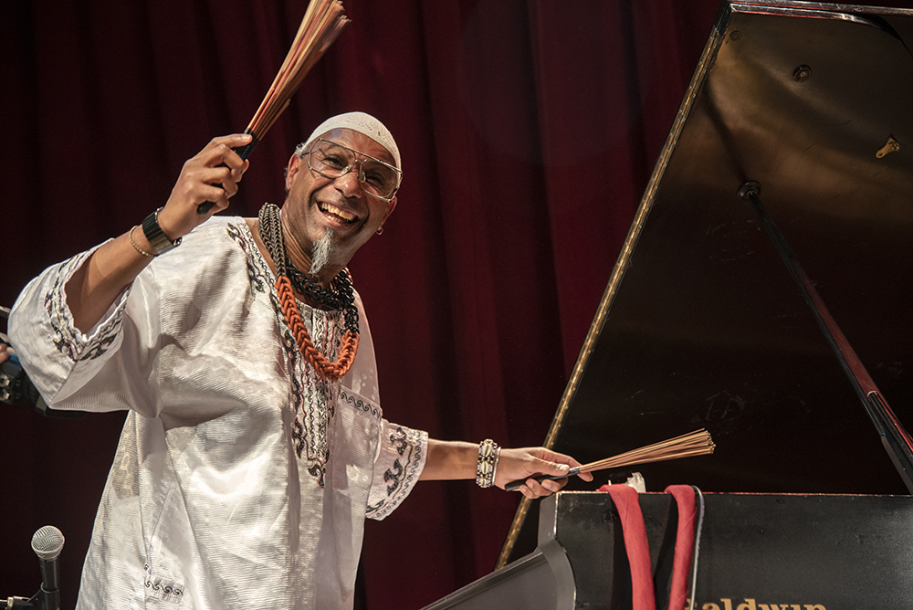 An action shot of Omar Sosa performing, playing the piano. (Smiling at the camera)