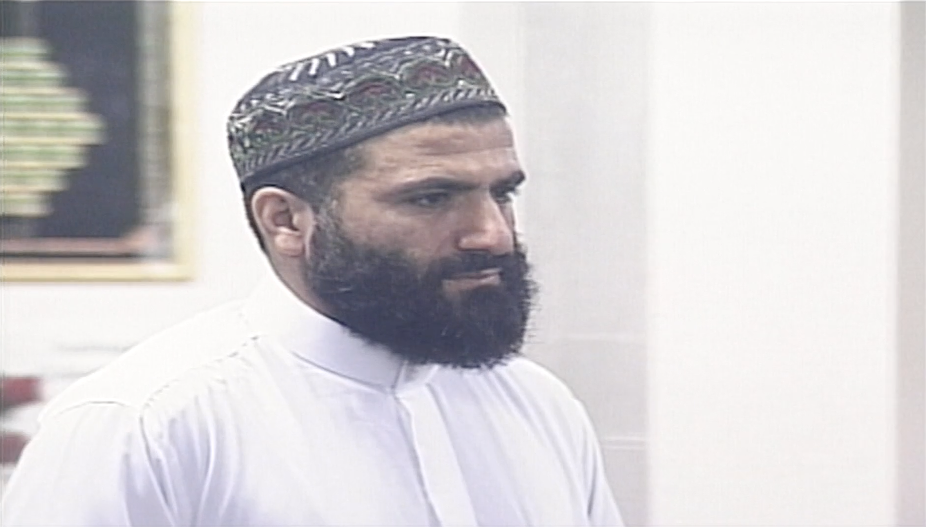 A close up of a man waering an Omani cap (or a Kuma) with a black beard and white shirt.