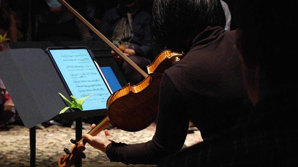 A behind shot of someone playing the violin and looking at sheet music on their iPad.