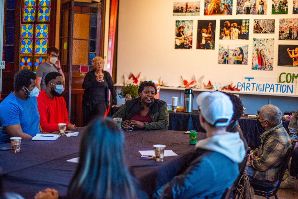 An image featuring Yoruba Richen talking to a table of people at the sanctuary.