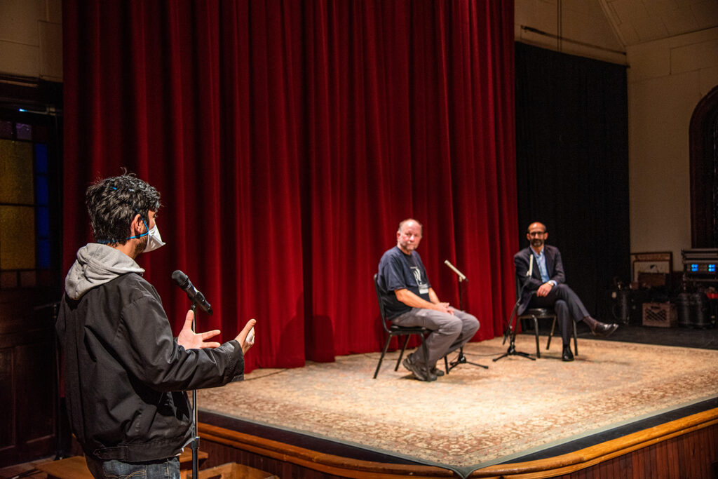 Shahan Mufti and Steve Pierce sitting on stage at at the Sanctuary with a questioner at the microphone off stage