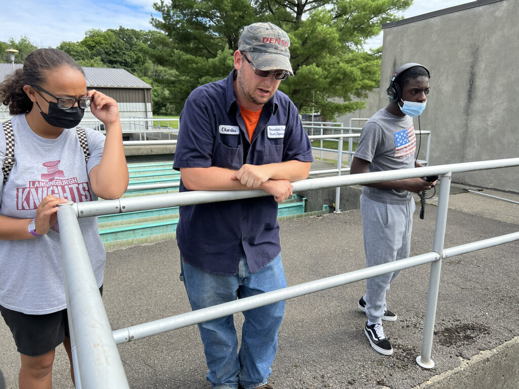 Charles Remington stands behind a railing with two Sanctuary youth fellows at the wastewater treatment plant.