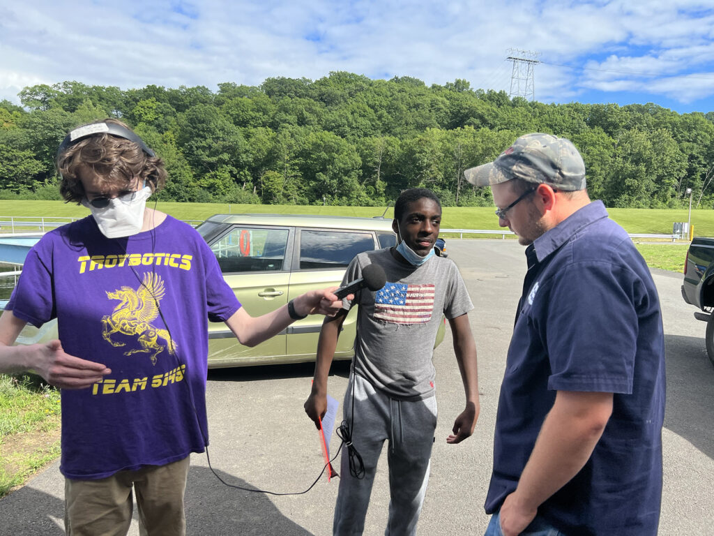 Outside in the parking lot, two Sanctuary youth fellows interview Charles with a microphone.