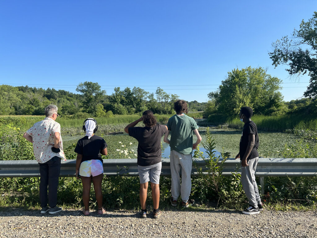 Five people stand behind a guard rail and look out at a marsh at the Papscanee Island nature preserve. 