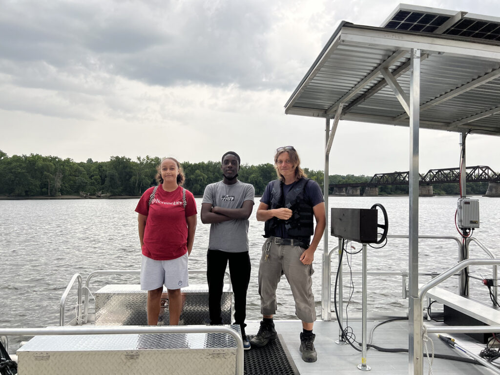 Scott and two Sanctuary youth fellows stand on the solar-powered pontoon boat on the Hudson River. 