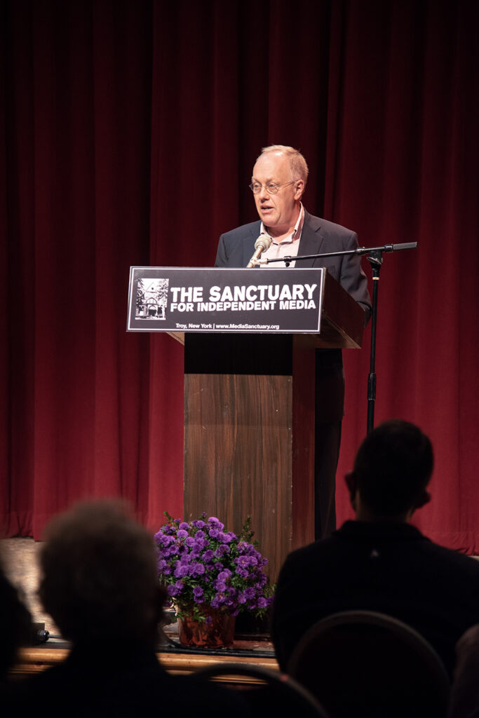 An image of Chris Hedges standing at the podium for the Sanctuary for Independent Media
