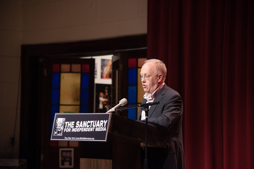 An image of Chris Hedges standing at the podium for the Sanctuary for Independent Media