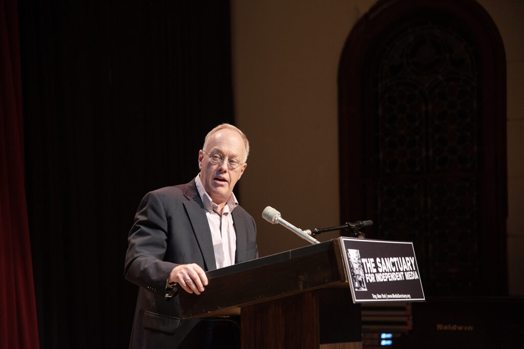 An image of Chris Hedges standing at the podium for the Sanctuary for Independent Media.