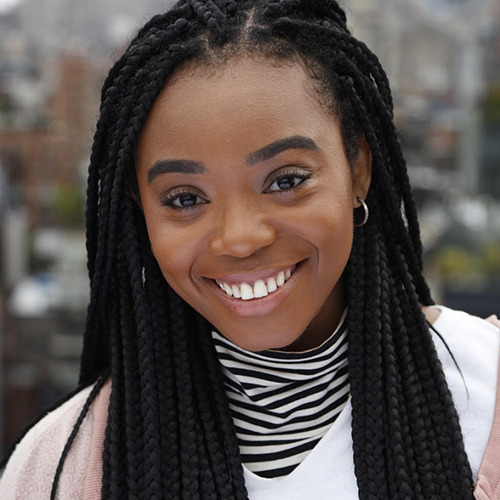 A head shot of Nile Assata Narris, the leader and actor featured in the event. She is a dark-skinned woman with long black braids and is smiling for the camera