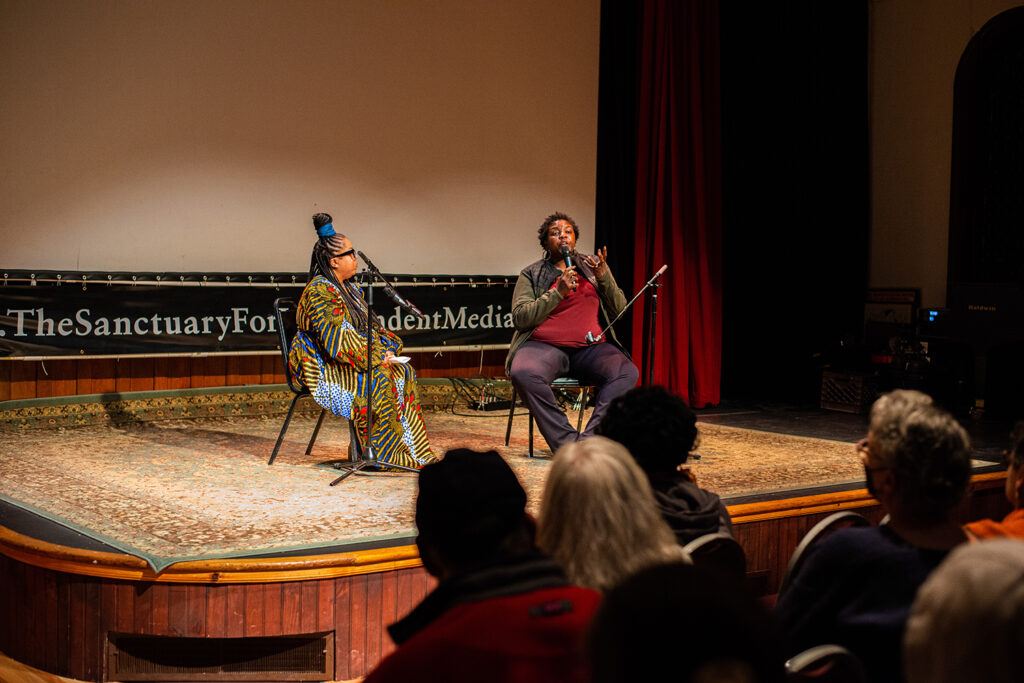 An image of Yoruba Richen and Dr. Veneilya Harden- Richen is speaking into the microphone.