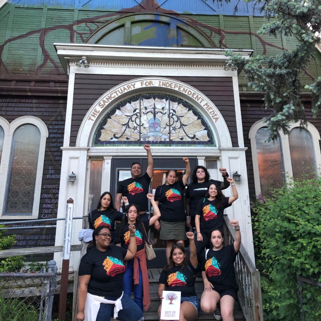 Barrio Alegria stands on the Sanctuary front steps, fists raised, and wearing Sanctuary tshirts.