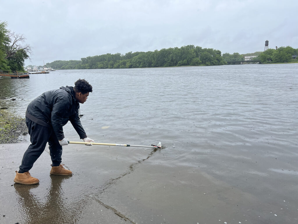 A Sanctuary youth fellow uses a pole to collect a water sample from the Hudson River. 