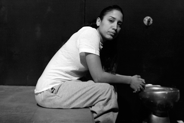 Black and white image of one of the prisoners in a white tee and grey sweats, looking into camera with a solemn face.