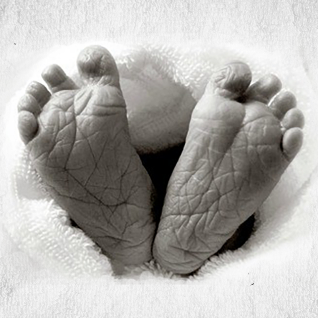 Baby feet with the heels touching (mimicking a heart shape) peek out from a white terrycloth towel
