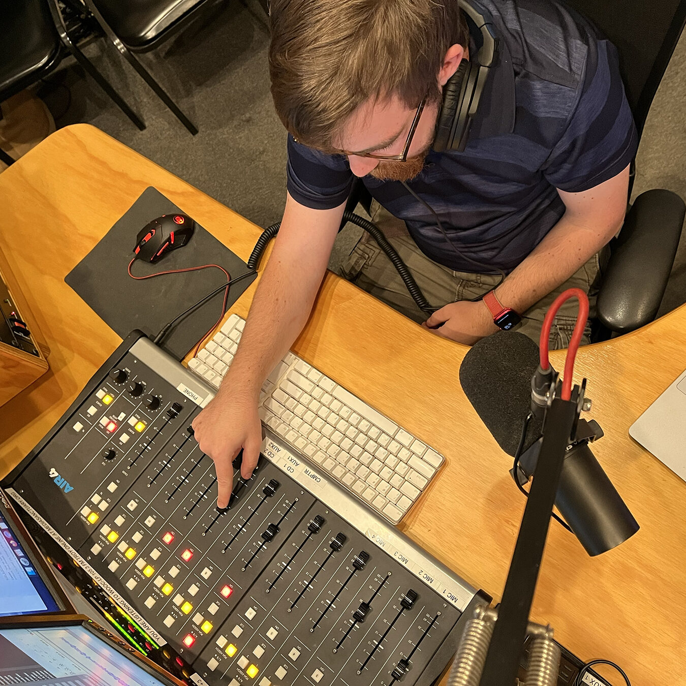 A high angle photo of Caelan McPherson at the soundboard in the radio studio. His finger is moving the fader