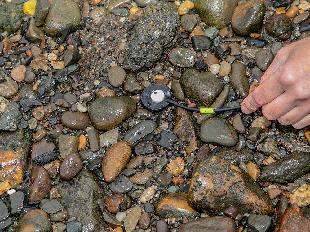 a contact mic (looks like a small disc attached to a cord) between wet rocks and a hand placing the mic