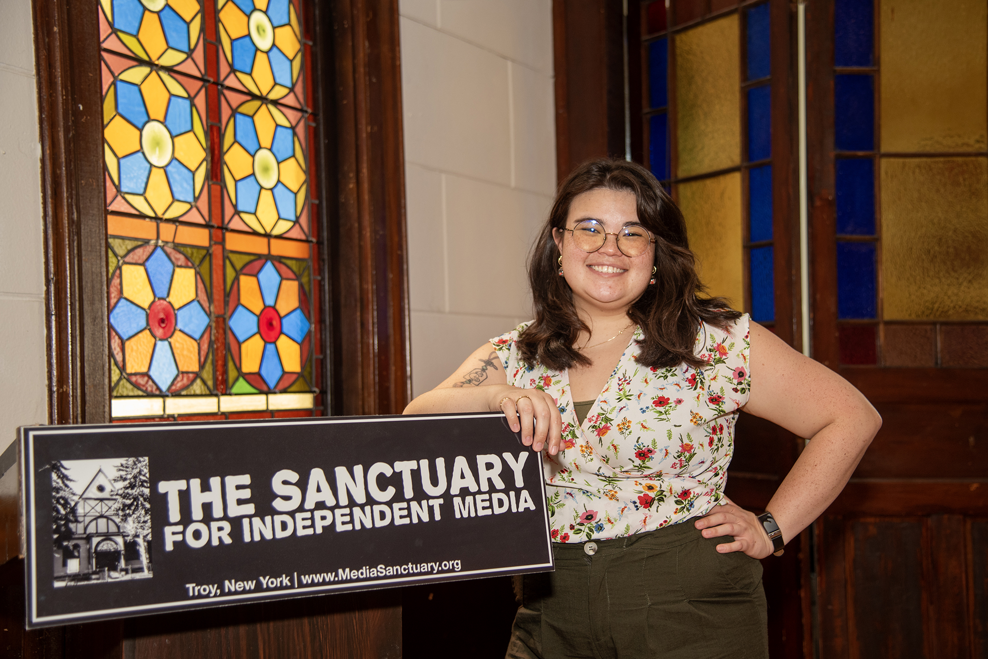 Ren Lee looks at the camera and smiles while leaning on the Sanctuary podium with stained glass windows in the background