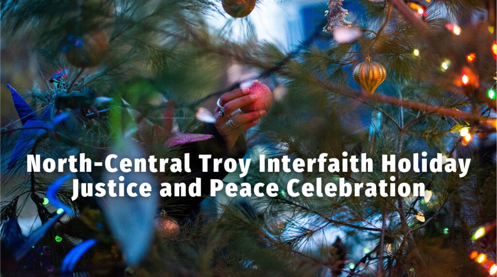 a had puts a holiday ornament in the evergreen tree. white text says, north-central troy interfaith holiday justice and peace celebration