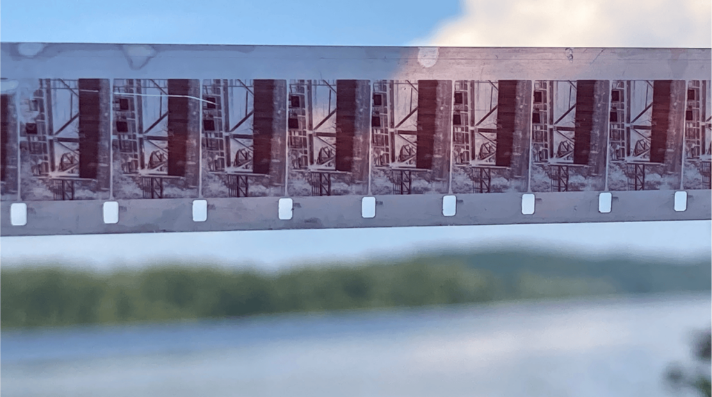 a photo of a strip of 16mm film held up against the sky with some blurry landscape in the background