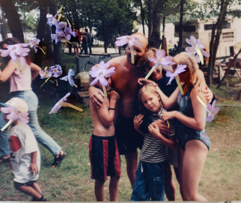 a photograph of a family in a big hug. over the image is purple flowers laid on the faces
