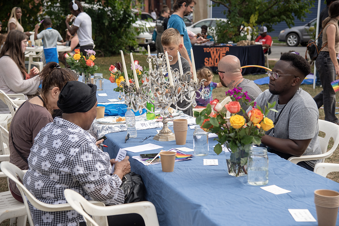 A long table with candles, flowers, and food, surrounded people in conversation