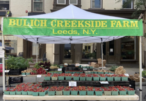 A text at the farmers' market, with a banner that says "Bulich Creekside Farm • Leeds, NY"