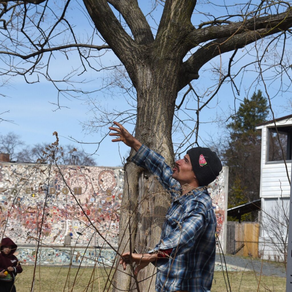 a photo of Christian in early spring at Freedom Square gesturing to a tree during the pruning and grafting workshop